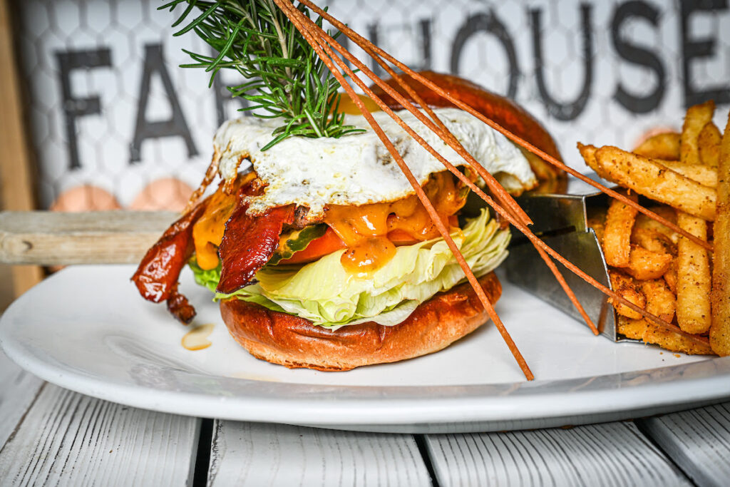 Hangover Burger off the new fall menu is stacked with bacon, cheddar, lettuce, tomato, and egg, served with fries at Hash House A Go Go Orlando on International Drive.