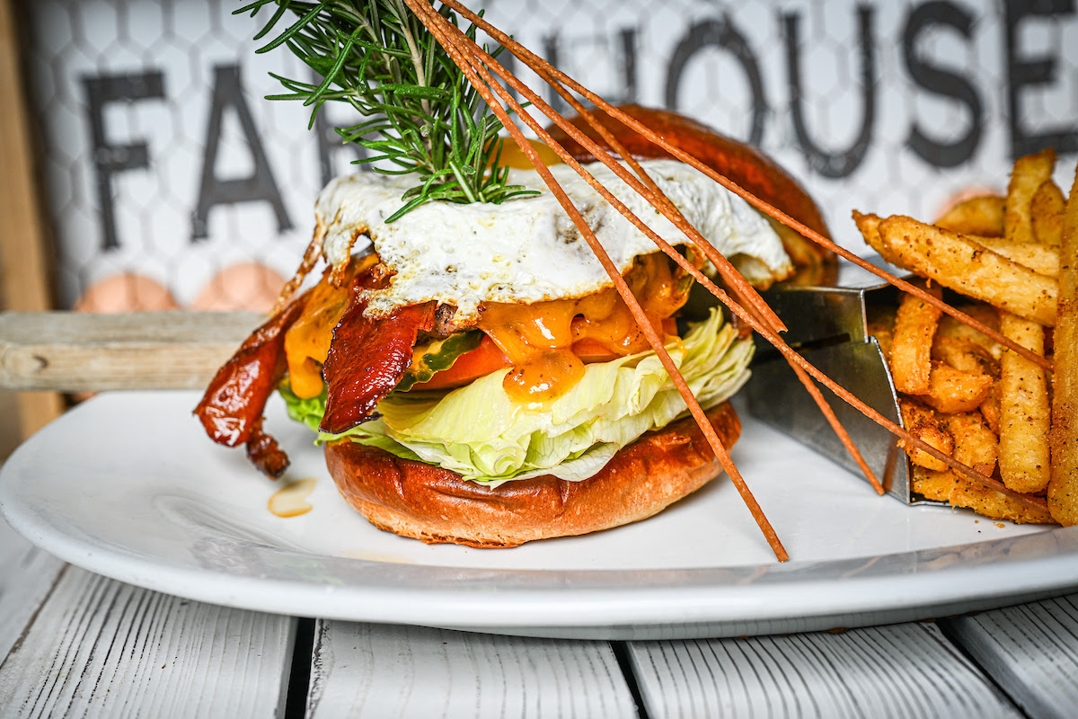 Hangover Burger off the new fall menu is stacked with bacon, cheddar, lettuce, tomato, and egg, served with fries at Hash House A Go Go Orlando on International Drive.